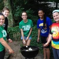 5 women around a grill smiling and roasting marshmallows